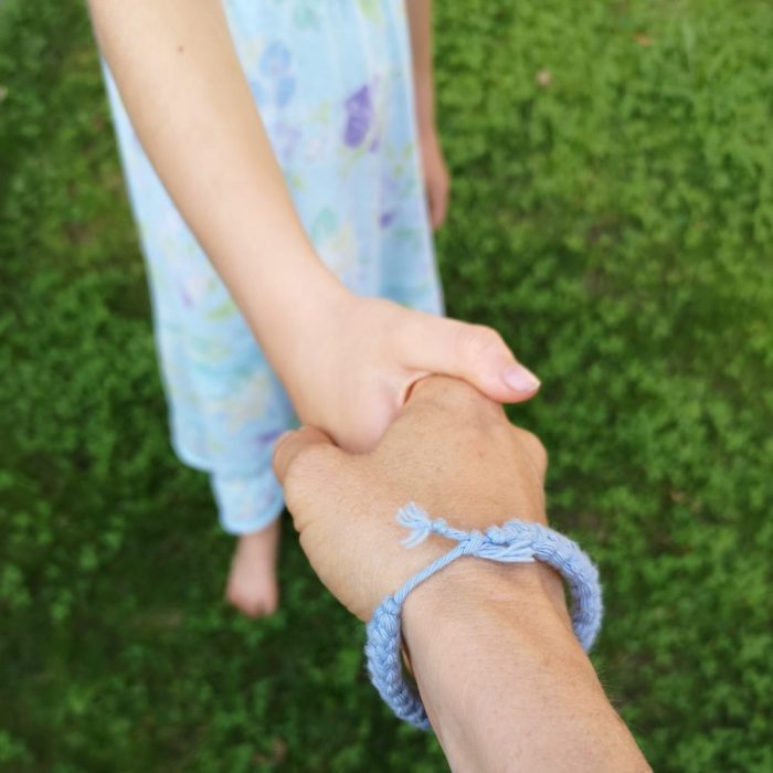Eine erwachsenen Hand hält die Hand eines Kindes in blauem Kleid.