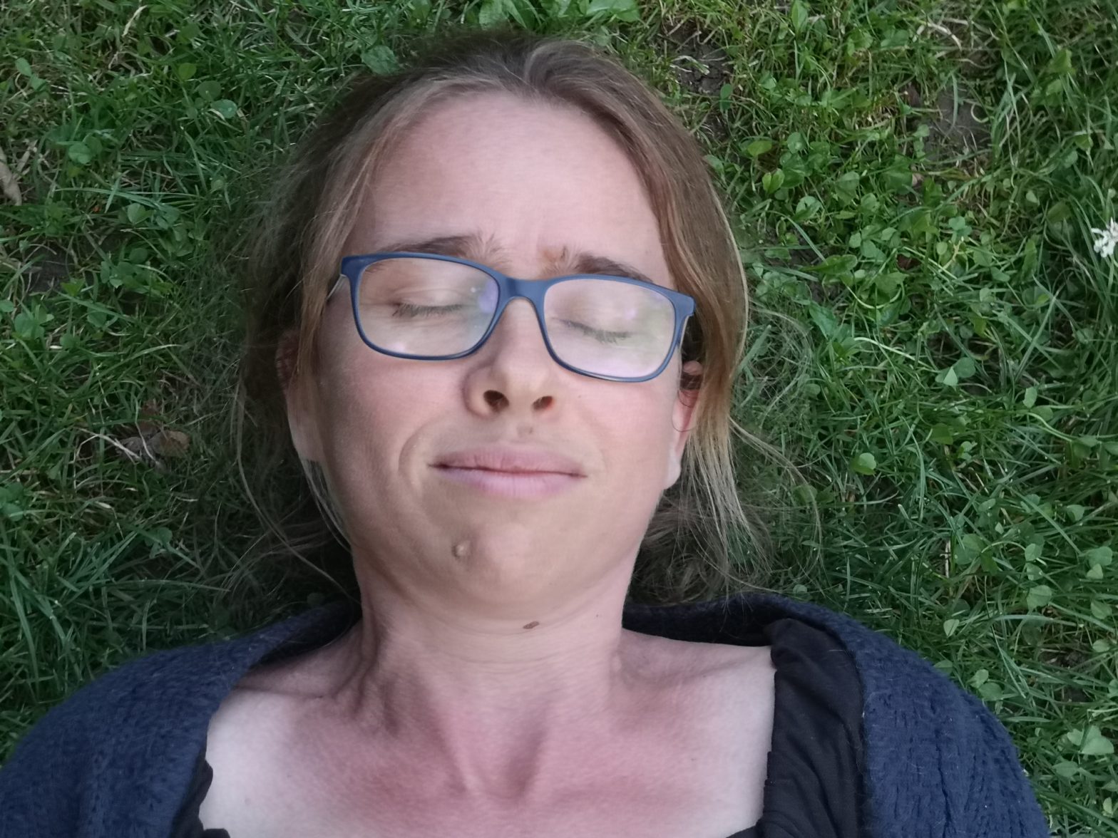 Eine Frau liegt mit geschlossenen Augen entspannt auf einer Wiese.